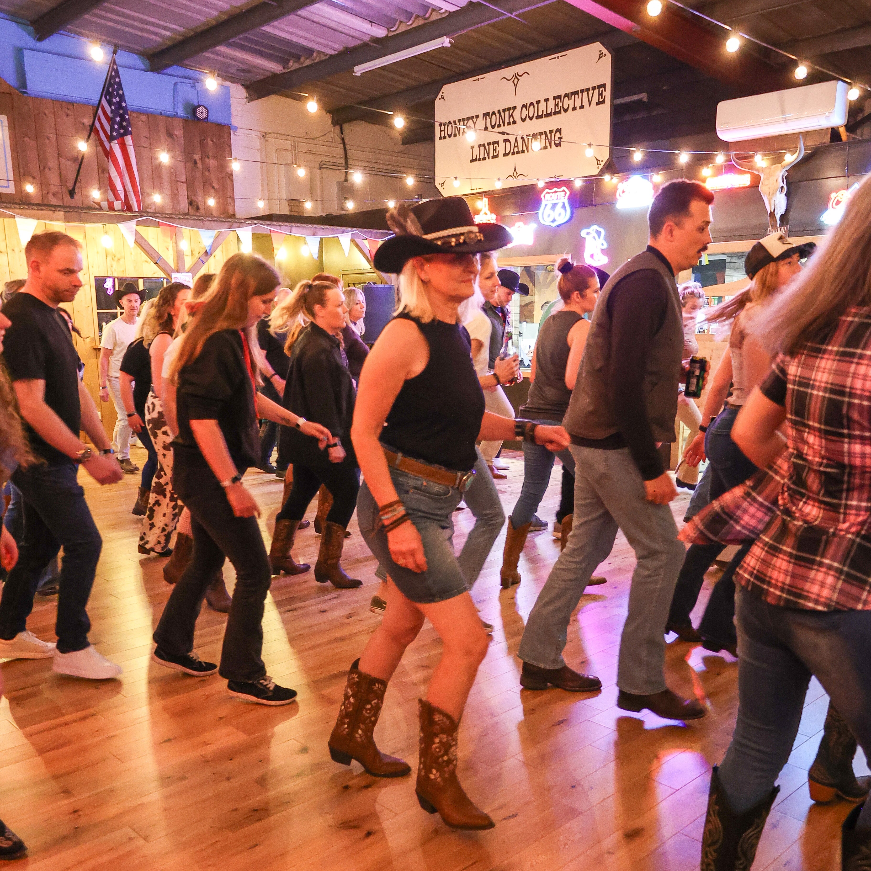 People dancing in a lively social setting with wooden floors and American flags.
